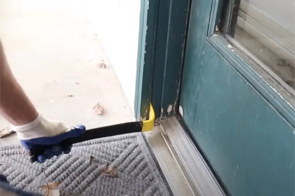 A gloved hand levering a sliding door panel out of its worn bottom track